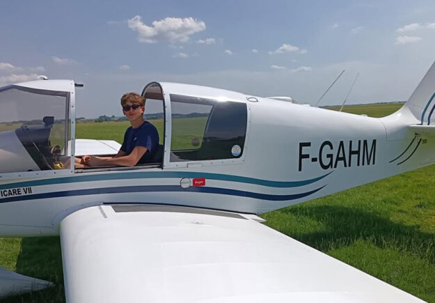 Un jeune pilote nommé Antoine assis dans le cockpit ouvert d'un avion de tourisme blanc immatriculé F-GAHM, sur la piste en herbe de l'Aéroclub de l'Aisne.