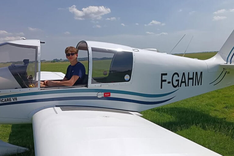 Un jeune pilote nommé Antoine assis dans le cockpit ouvert d'un avion de tourisme blanc immatriculé F-GAHM, sur la piste en herbe de l'Aéroclub de l'Aisne.