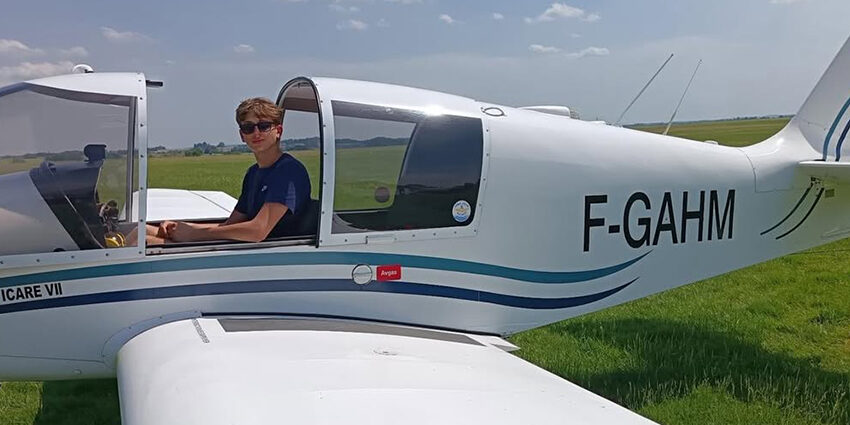 Un jeune pilote nommé Antoine assis dans le cockpit ouvert d'un avion de tourisme blanc immatriculé F-GAHM, sur la piste en herbe de l'Aéroclub de l'Aisne.