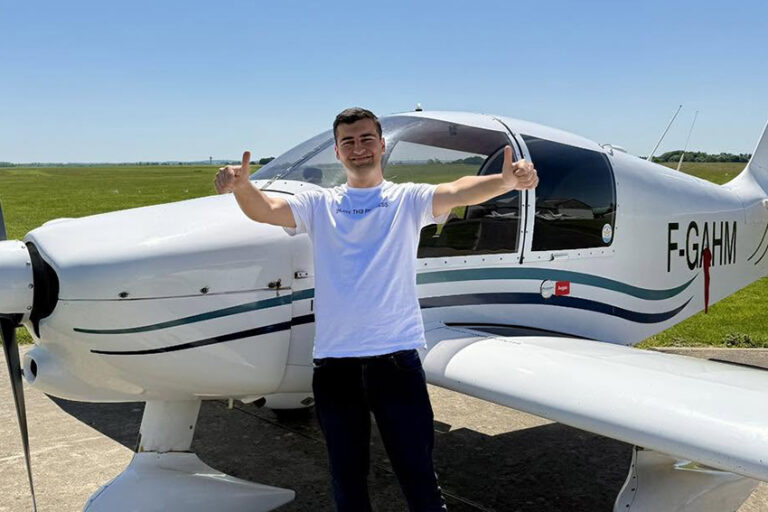 Le jeune pilote Serdem souriant, faisant un double pouce levé devant un avion de tourisme blanc immatriculé F-GAHM sur le tarmac ensoleillé de l'Aéroclub de l'Aisne.